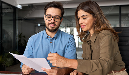 Un hombre con gafas y una mujer con camisa verde oliva revisan atentamente un documento impreso en una oficina moderna, mostrando un ambiente de trabajo colaborativo.