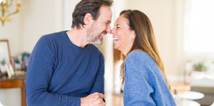 Primer plano de un hombre y una mujer de mediana edad riendo con alegría, con sus rostros muy cerca el uno del otro en un momento de complicidad y afecto.