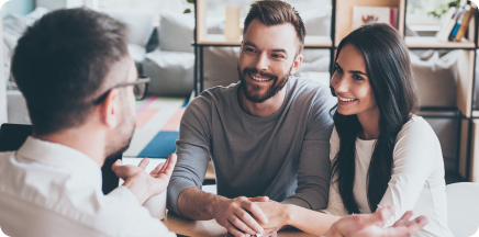 Una pareja joven sentada frente a un asesor profesional en una oficina moderna y luminosa, compartiendo risas y una conversación de confianza durante una consulta.